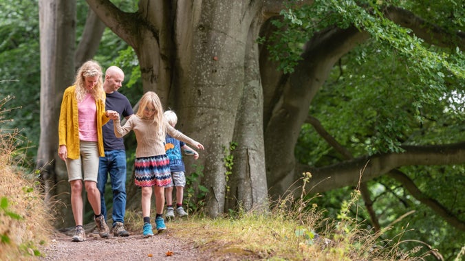 A family walking down a path towards the camera, surrounded by trees and foliage